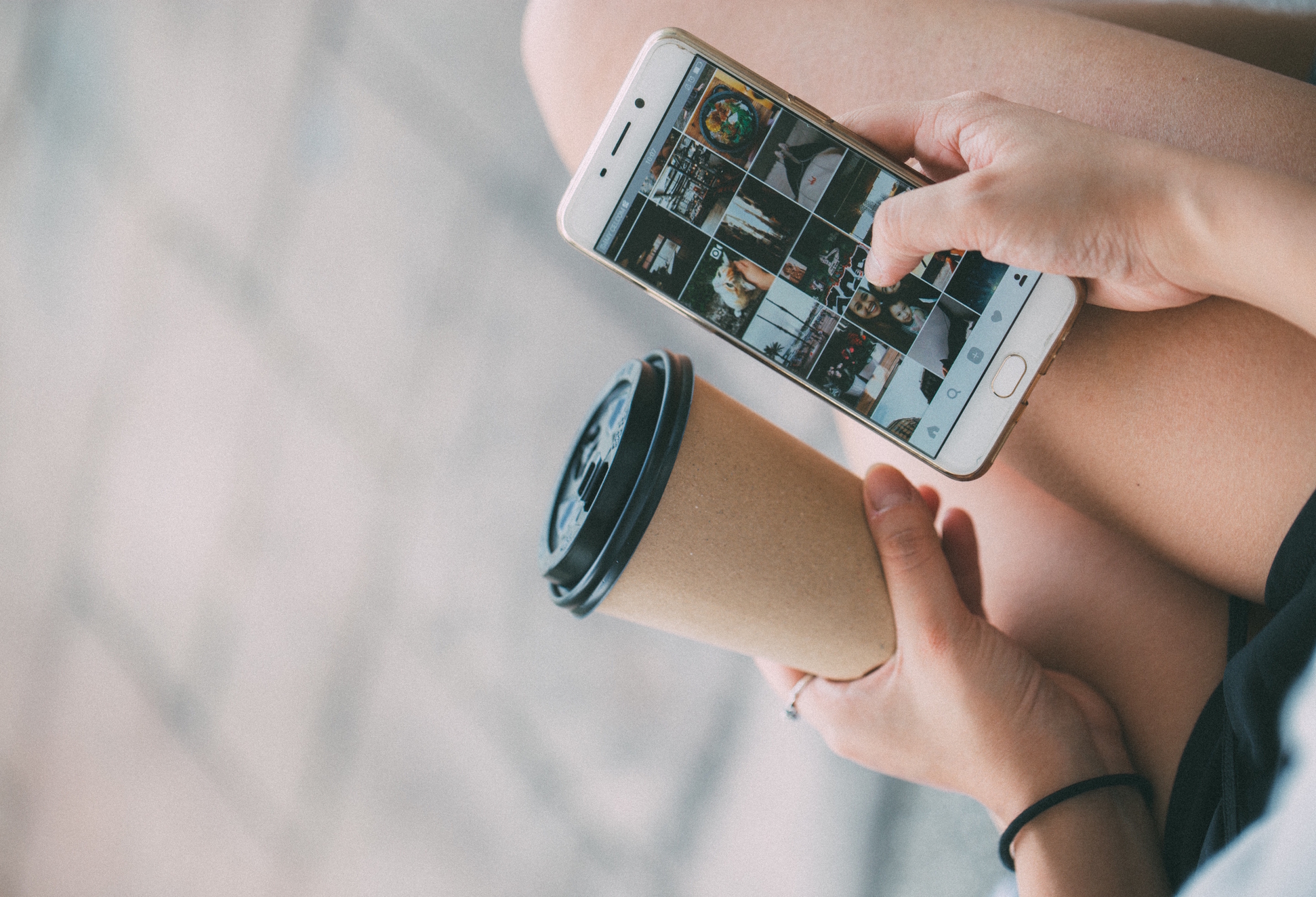 Girl holding coffee browses Instagram on an iPhone