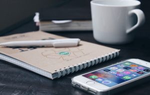 iPhone lays on an agency desk next to a coffee cup and notepad
